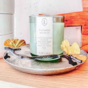 Luxe Intuition Farmers Market candle on a gold ginkgo-leaf tray against marble and wood