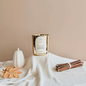 Wick & Bloom Autumn Sunday candle with a white pumpkin, an autumn leaf and wood sticks on cream linen
