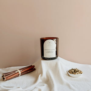 Wick & Bloom Cardamom Cashmere candle with wood sticks and a dish of cardamom pods on cream linen