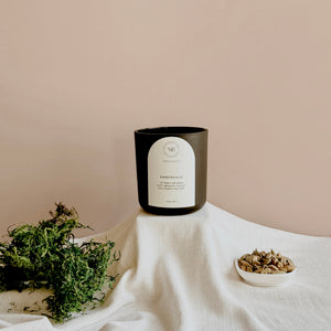 Wick & Bloom Emberhaus candle with moss and a dish of cardamom pods on cream linen