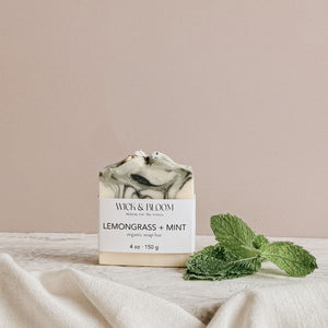 Wick & Bloom Lemongrass + Mint organic soap bar on cream linen with fresh mint leaves, dusty pink background