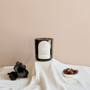 Wick & Bloom Orris & Smoke candle with a black iris flower and a dish of resin on cream linen