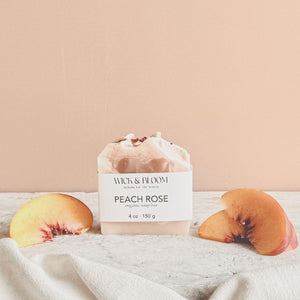 Wick & Bloom Peach Rose organic soap bar on white cloth with fresh peach slices, soft peach-pink background
